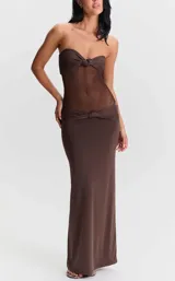 Vestido largo color marrón de silueta entallada, con tirantes finos, escote pronunciado con detalle de nudo y sección translúcida en la zona del torso con malla transparente.