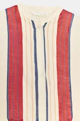 Vestido túnica semitransparente de cuello redondo y manga larga, de color crudo con detalles de rayas rojas, azules y beige en el pecho y el bajo. Cuenta con aberturas laterales y cierre frontal con botones.