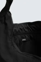 Bolso de hombro tipo hobo fabricado en tejido técnico de nylon. Cuenta con un compartimento principal con cierre de cremallera, un bolsillo interior con cierre y un asa ajustable con detalle de mosquetón.