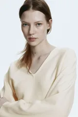 Remera de punto fino suave color beige, con escote en V, cintura entallada y mangas dolman largas.