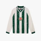Camiseta de manga larga estilo jersey de fútbol, con diseño a rayas verticales alternando blanco y encaje verde. Presenta cuello polo con detalles en blanco y verde, y un escudo circular bordado en el centro del pecho con una rosa.