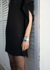 Vestido corto negro de tejido fluido con diseño evasé, cuello alto y mangas cortas asimétricas con volantes.