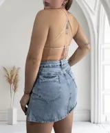 Top halter de crochet tejido en punto bajo, color rosa pálido con sutil brillo. El diseño es de forma triangular invertida, ajustado al busto y con tiras finas para atar al cuello.