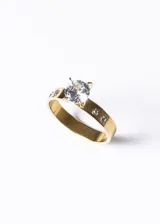 Anillo dorado de acero quirúrgico con circonia central y pequeñas circonias engarzadas en el aro.