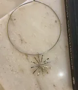 Gargantilla rígida de metal con dije central en forma de sol con rayos alargados y textura martillada.