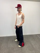 Pantalón de jean azul raw con diseño de corte versátil, ajustable mediante cierres laterales que revelan un panel interior rojo. Presenta una estampa gráfica de gran tamaño en la parte trasera con detalles bordados, costuras reforzadas y etiqueta de cuero en la cintura.