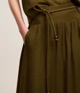 Pollera midi evasé color verde militar, confeccionada en crepé. Cuenta con cintura ancha elástica en la parte trasera, trabillas en los laterales y cinturón de cuerda incorporado con abalorios en las puntas.