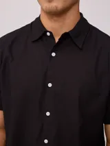 Camisa de manga corta color negro, con cuello clásico y cierre frontal de botones.