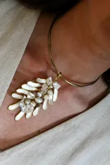 Gargantilla rígida dorada con dije colgante de forma irregular con incrustaciones de perlas y nácar.