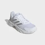 Championes deportivos Adidas modelo Courtjam Control 3, color blanco con tres franjas plateadas brillantes en los laterales. Presentan una construcción robusta con puntera reforzada y suela gruesa para soporte en canchas de arcilla.