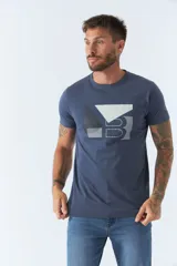 Remera de hombre color azul, con cuello redondo y manga corta. Presenta un diseño gráfico estampado en el frente con formas geométricas y letras en tonos blanco y gris.
