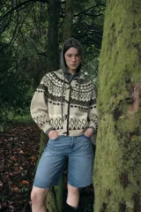 Chaqueta de punto con diseño jacquard de estilo nórdico, en tonos beige, marrón y blanco. Presenta capucha, cierre frontal con botones tipo trenca y mangas largas con puños ajustados.