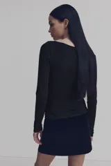 Top de manga larga en punto, color negro, con escote asimétrico, detalle girado en el frente y frunces laterales que crean un efecto drapeado.