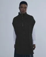 Chaleco largo de punto trenzado color gris con cuello alto y cierre frontal con cremallera metálica.