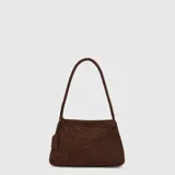 Cartera tipo shoulder bag de color marrón, confeccionada con diseño trenzado y textura de gamuza. Cuenta con un asa única trenzada y un pequeño llavero colgante en el lateral.