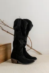 Bota estilo tejana de caña alta, confeccionada en gamuza, con taco cuadrado y diseño de costuras decorativas.