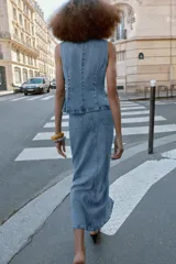 Chaleco de denim con cuello redondo y diseño sin mangas. Presenta un cierre frontal cruzado con botones y falsos bolsillos de vivo en la parte delantera.