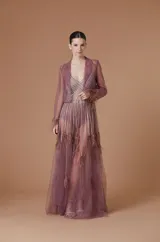 Vestido largo de tul color malva, compuesto por un body con escote en V y aplicaciones de tiras brillantes, cubierto por una capa transparente de tul con detalles de plumas en los puños y el ruedo.