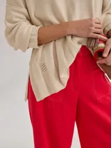 Buzo de tejido de punto liviano en color beige, con escote en V y diseño holgado. Presenta costuras visibles en los hombros y un detalle bordado en el lateral inferior.