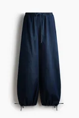 Pantalón tobillero de corte holgado en denim suave, con tiro bajo, elástico revestido en la cintura, cordón de ajuste y bolsillos laterales. Presenta diseño de piernas globo con cordón ajustable en los bajos.