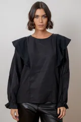 Blusa blanca de algodón con cuello redondo, mangas largas con puños elásticos y volados decorativos en los hombros.