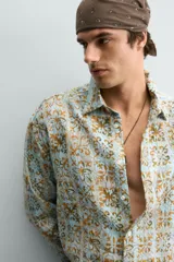 Camisa de corte relajado confeccionada en tejido fluido con estampado geométrico en tonos azules y ocres. Presenta cuello solapa, cierre frontal de botones y manga larga con puños abotonados.