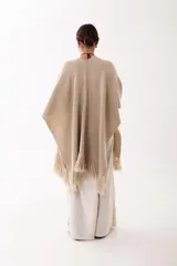 Ruana de tejido de punto en color beige, con diseño abierto y terminaciones con flecos en los bordes.