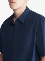 Camisa azul marino de manga corta, con cuello clásico, cierre frontal con botones, bolsillo de parche en el pecho izquierdo y logo CK bordado en el bolsillo.