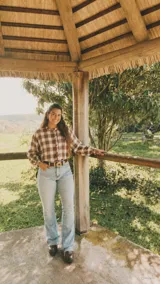 Camisa de viyela con estampado de cuadros en tonos marrones y crudos. Presenta cuello redondo con volados, cierre frontal de botones y mangas largas con puños ajustados.