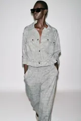 Chaqueta jaspeada color beige, con cuello solapa, manga tres cuartos con trabilla y botón, bolsillos delanteros de plastrón con solapa, bajo ajustable con cordones interiores y cierre frontal con botones a presión.