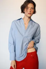 Camisa de manga larga en color celeste con estampado de rayas finas, cuello solapa y escote en pico con detalle de solapa frontal. Presenta puños abotonados y bajo asimétrico.