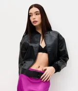 Campera bomber de cuero sintético negro, con cierre frontal de cremallera, cuello alto y puños y bajo elásticos con rib. Presenta costuras decorativas en los hombros.