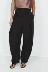 Pantalón negro de tiro alto, corte amplio estilo balloon o culotte, con pliegues marcados en el delantero y bolsillos laterales ocultos.