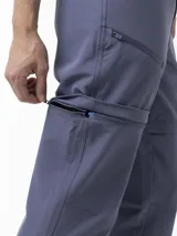 Pantalón Merrell desmontable de trekking color gris, de corte recto y tiro medio, confeccionado con tejido elástico de poliéster y spandex. Incluye cinturón ajustable, bolsillos laterales con cierre y logo reflectante.