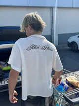 Camisa de waffle color crema con cuello polo, mangas cortas y bordado marrón en la espalda.