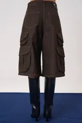 Bermuda cargo de tiro medio confeccionada en denim color marrón oscuro. Presenta un diseño amplio con bolsillos laterales tipo cargo con solapa y bolsillos delanteros clásicos, cierre frontal con cremallera y botón.