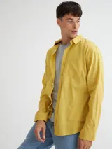 Camisa manga larga amarilla de algodón con bolsillo en el pecho, botones de pasta, logo bordado en el ruedo y etiqueta de marca en la tapeta de botones.