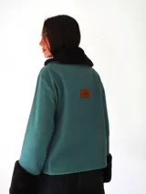 Campera de gamuza color beige con interior y detalles de corderito sintético en cuello y puños. Presenta cierre frontal con botones tipo toggle de madera y cuero, y bolsillos frontales.