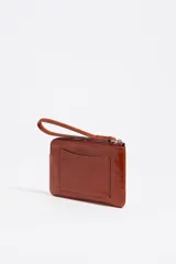 Monedero de piel color marrón rojizo con acabado brillante, estructura rígida y cierre de cremallera con tirador de tejido. Presenta logo metálico de Bimba y Lola en el frente y bolsillo interior.