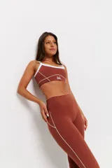 Conjunto deportivo de dos piezas color chocolate con detalles de costuras blancas. Incluye un top de tirantes finos con escote redondo y un pantalón largo de corte ajustado con aberturas en el bajo.