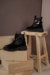 Bota tipo Chelsea de cuero marrón con suela track negra de goma. Presenta paneles elásticos laterales y una costura reforzada en la puntera. Incluye una correa de cuero desmontable con hebilla metálica.