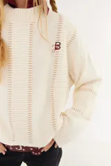 Sweater de punto color beige, con diseño de textura acanalada en mangas y espalda, cuello polo en color bordó y parche decorativo en la parte superior de la espalda.