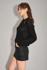 Minifalda negra de tiro medio, confeccionada en material con acabado engomado o efecto cuero, con diseño de cinco bolsillos y cierre frontal con botón y cremallera.