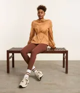 Campera deportiva femenina tipo parka, color ocre, confeccionada en poliamida y poliéster. Tiene cuello con capucha, mangas largas con puños elásticos, cierre frontal con cremallera y cordón ajustable en la cintura.