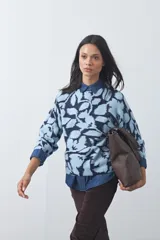 Sweater de punto con diseño estampado de hojas en tonos azul claro y azul oscuro. Presenta cuello redondo, mangas largas y terminaciones acanaladas en puños y ruedo.