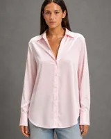 Camisa de satén rosa de manga larga, con cuello clásico, cierre frontal de botones y puños abotonados. Presenta un corte recto y fluido con ruedo redondeado.