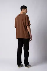 Remera de corte oversized en color marrón, confeccionada en tejido de algodón con textura de micropanal. Presenta cuello redondo con detalle de costura en forma de X y mangas cortas de estilo caído.