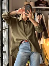 Camisa verde militar de corte oversize y largo asimétrico, con cuello clásico, mangas largas remangadas y cierre frontal con botones.