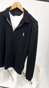 Sweater de punto negro con cuello polo, cierre de cremallera metálica y logo bordado en el pecho.