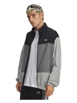 Campera deportiva Under Armour con cierre frontal completo, diseño de bloques de color en tonos negro y gris. Presenta cuello alto, bolsillos laterales con cierre y puños elásticos. Incluye tecnología UA Storm que repele el agua.